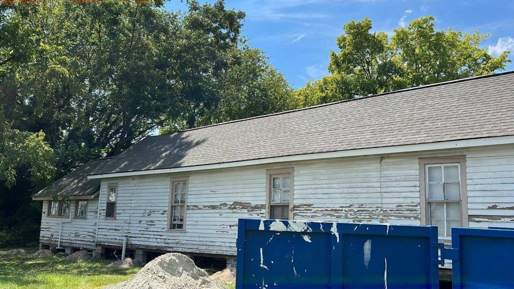 An Old White House With a Blue Dumpster in Front of It