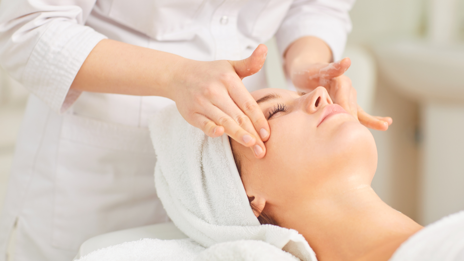 Spa therapist performing a facial massage on a client wearing a white towel headband