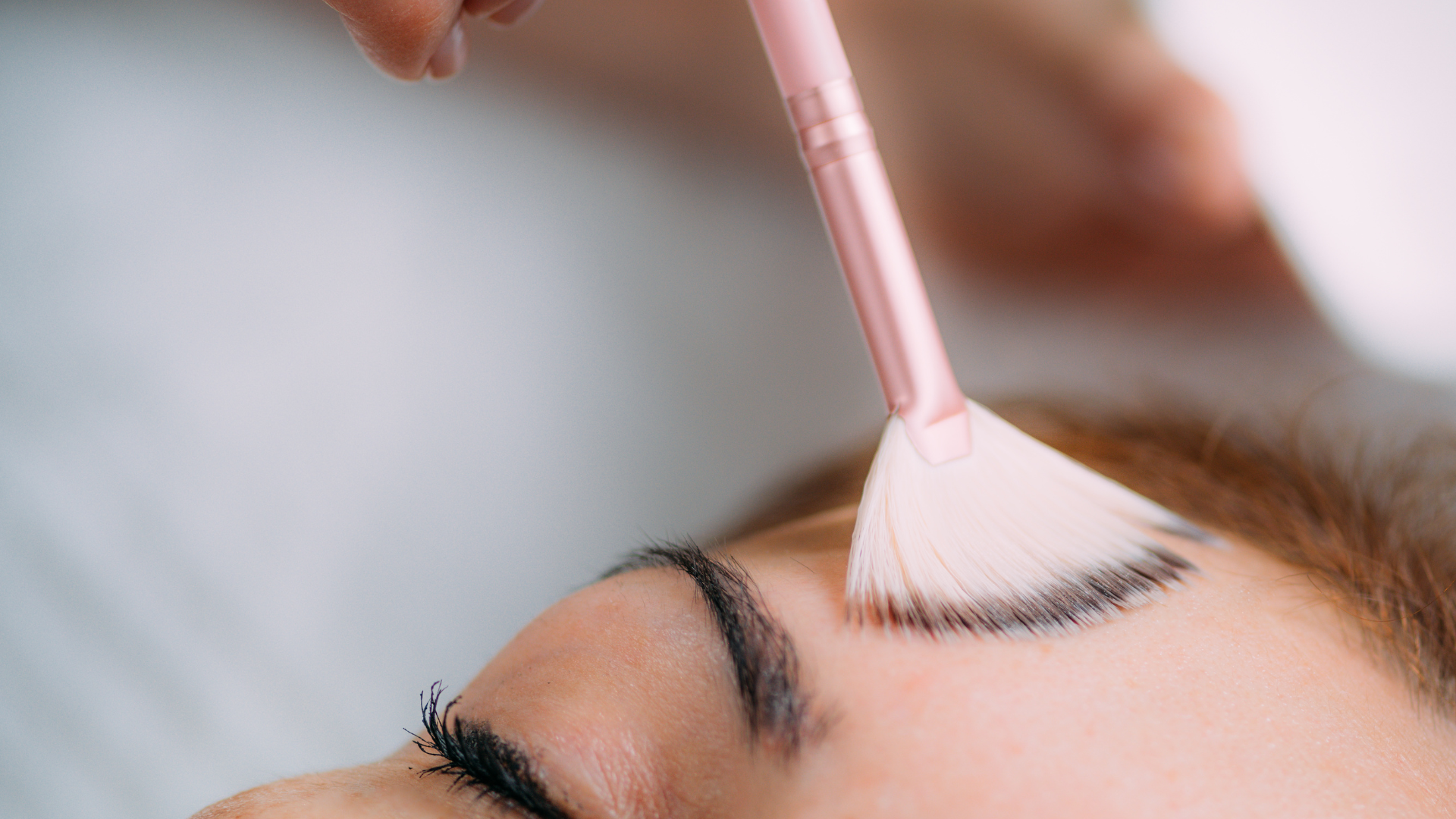 Makeup brush applying white eye shadow to a closed eyelid