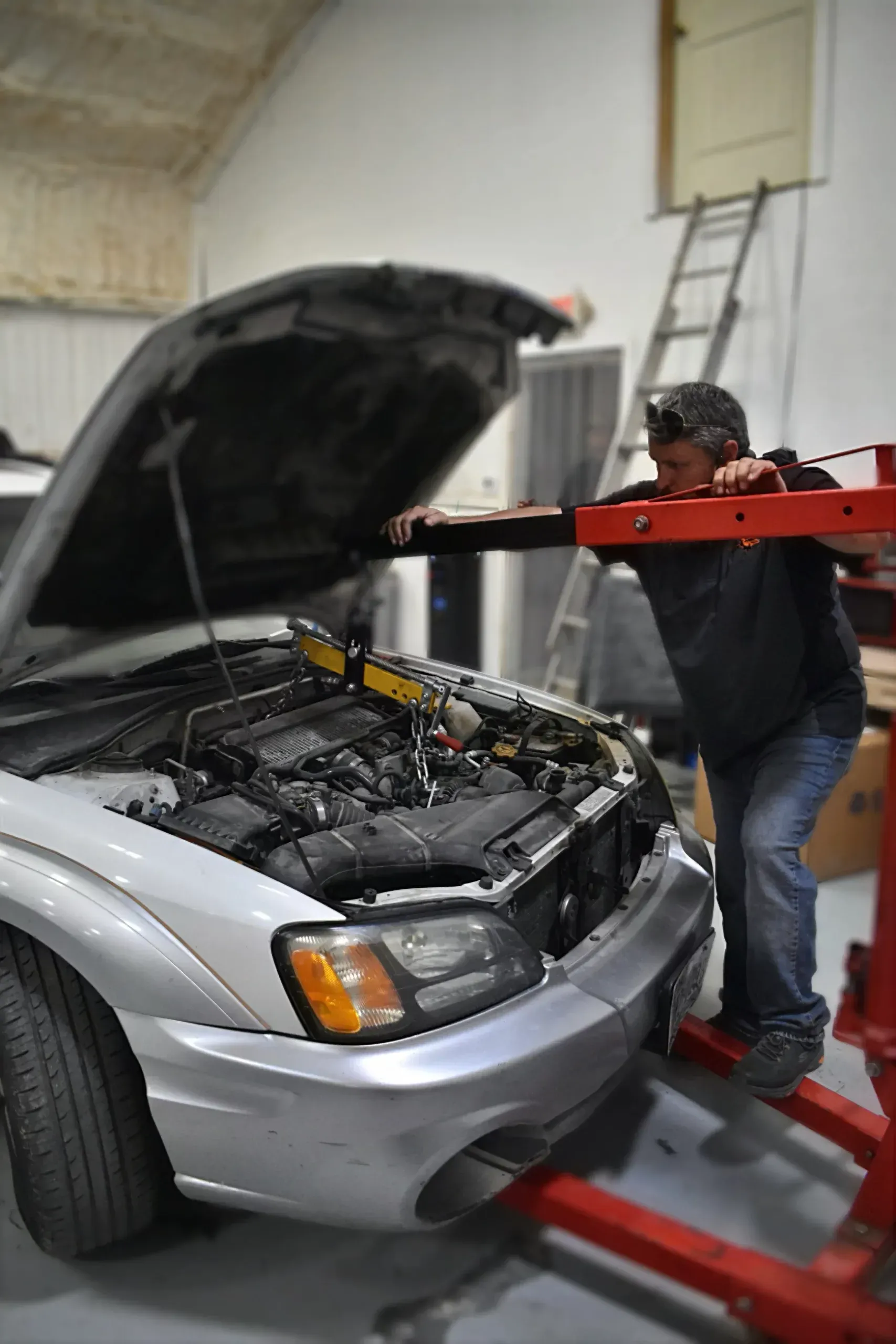 Mechanic inspecting a silver car’s engine on a red lift in a garage