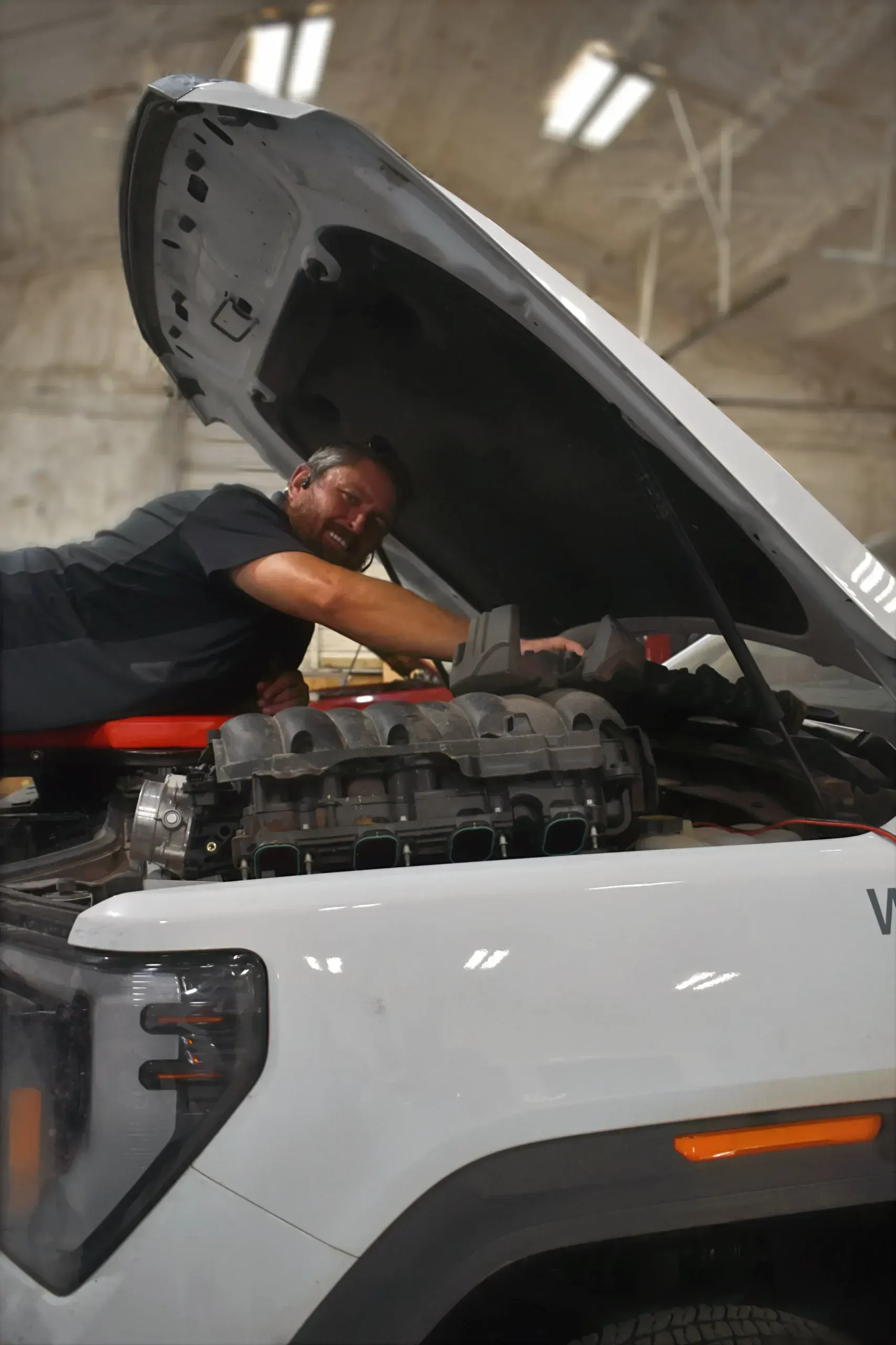 Person working under the open hood of a white pickup truck in a garage