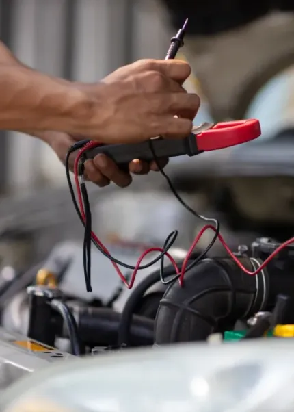 Hands using a multimeter to test wires in a car engine compartment