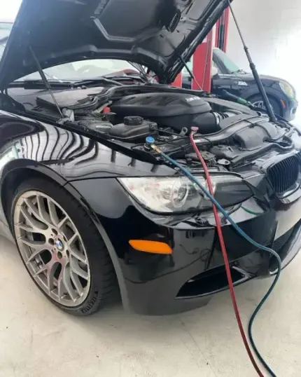 Black sports car with hood open in a garage, connected to jumper cables for maintenance or repair