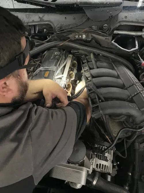 Mechanic inspecting a silver car’s engine on a red lift in a garage