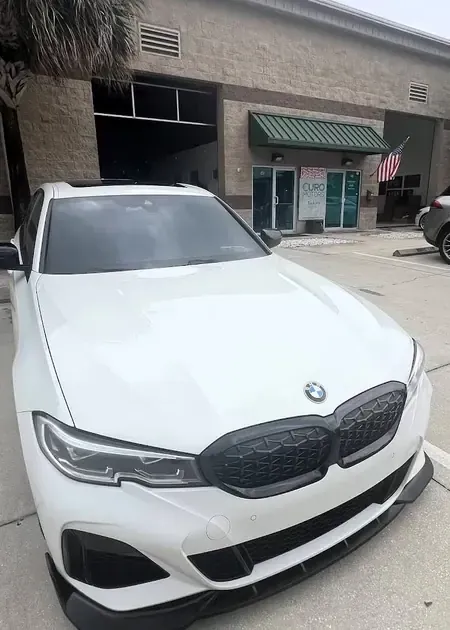 White BMW sedan parked on a road under an overcast sky