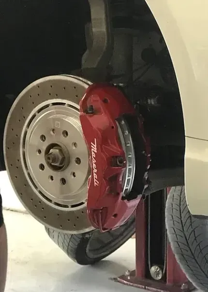 Close-up of a car wheel with a red brake caliper and drilled brake rotor on a lift