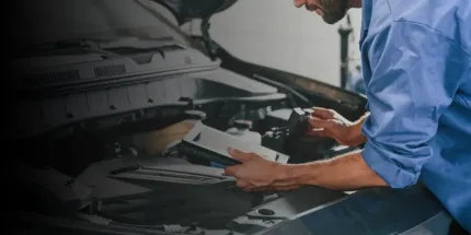 Mechanic in blue shirt inspecting a car engine with a handheld diagnostic device