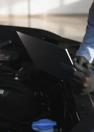 Mechanic holding a black car hood open inside a garage