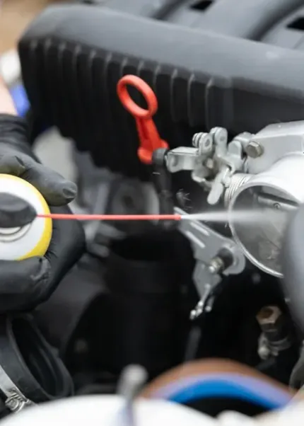 Close-up of a car engine bay with a red dipstick and a gloved hand using a red gauge tool