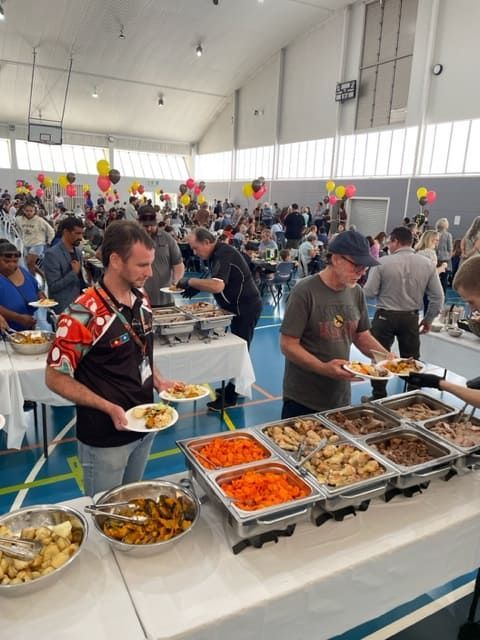 A Group Of People Are Standing Around Buffet Tables Eating Food — Tru Blu Catering In Woolgoolga, NSW