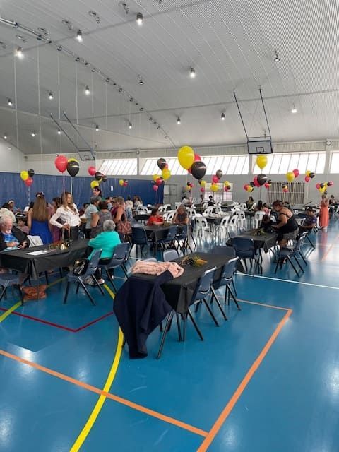 A Group Of People Are Sitting At Tables In A Gym With Balloons Hanging From The Ceiling — Tru Blu Catering In Woolgoolga, NSW