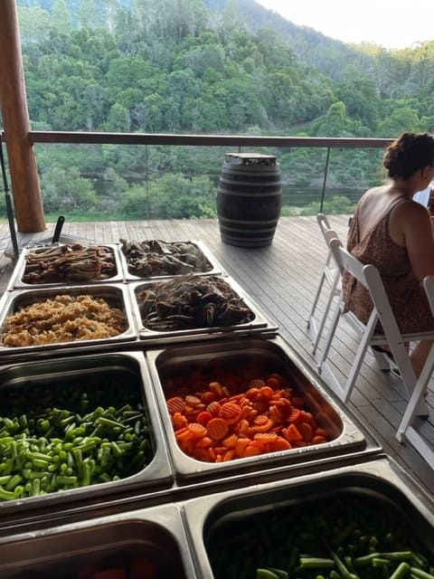 A Woman Is Sitting At A Table With A View Of A Forest Behind Her — Tru Blu Catering In Kempsey, NSW