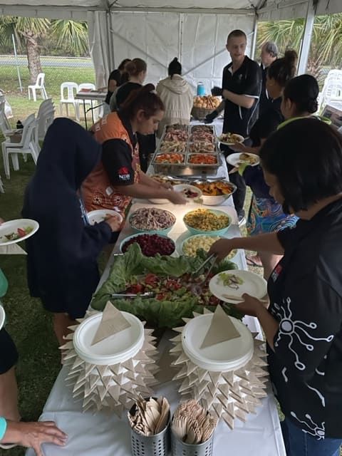 A Group Of People Are Standing Around A Table Eating Food — Tru Blu Catering In Wauchope, NSW