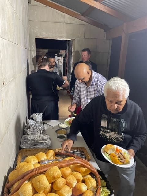 A Group Of Men Are Standing Around A Table Eating Food — Tru Blu Catering In Port Macquarie, NSW