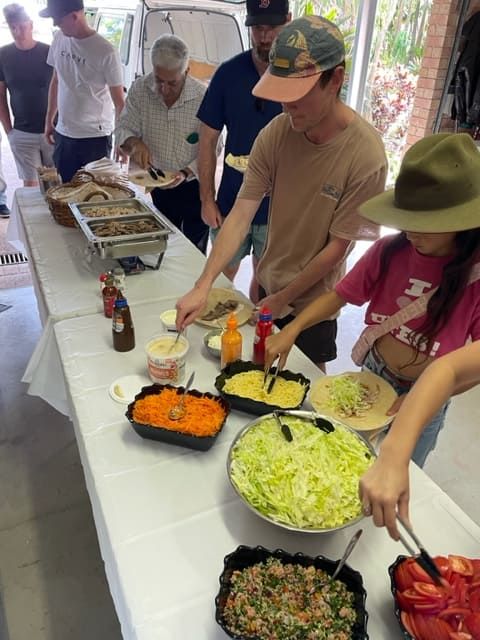 A Group Of People Are Standing Around A Table Eating Food — Tru Blu Catering In Port Macquarie, NSW