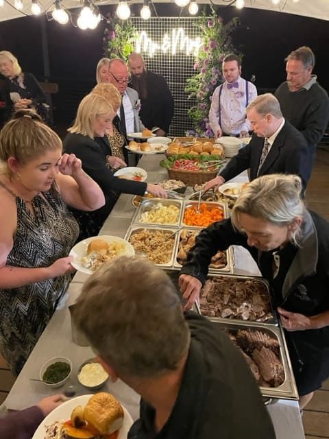 A Group Of People Are Standing Around A Buffet Table Eating Food — Tru Blu Catering In Port Macquarie, NSW