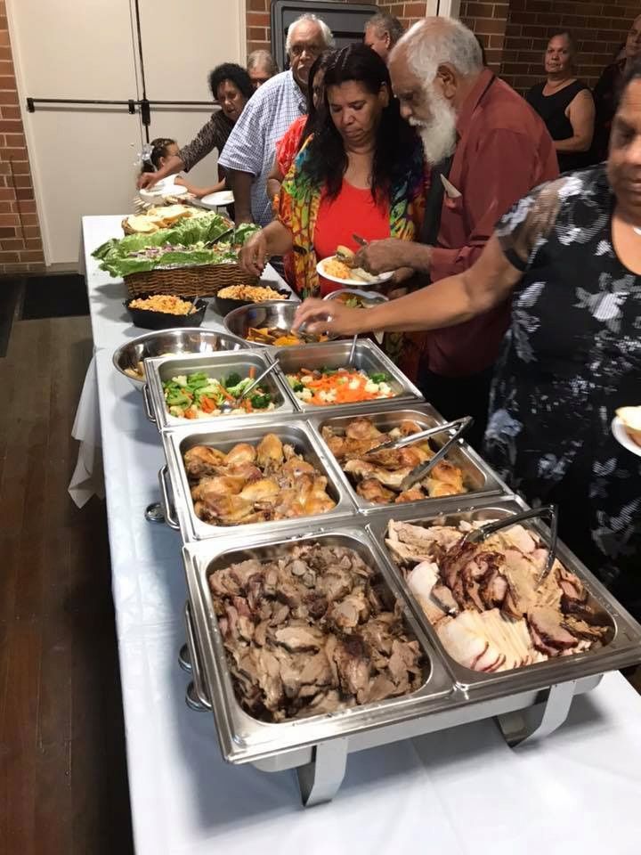 A Group Of People Are Standing Around A Buffet Table Eating Food — Tru Blu Catering In Woolgoolga, NSW
