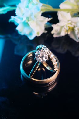 Two wedding rings on a dark surface with white flowers blurred in the background
