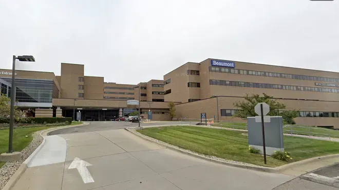 Hospital building entrance with driveway, grass, and blue signs on a cloudy day