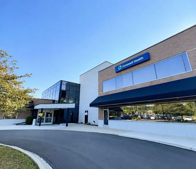 Modern building exterior with blue awnings, glass entrance, and clear sky above parking area