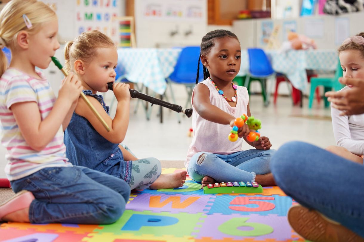 Children sitting on a classroom rug, clapping during a group activity in a preschool circle time.
