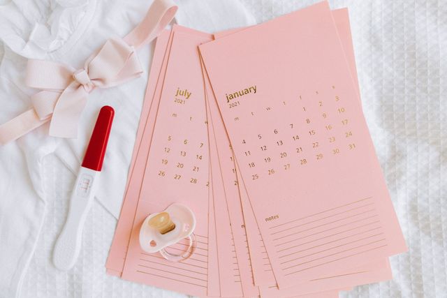 Pink monthly planner pages with a red pen, white ribbon, and small flower on a soft textured background