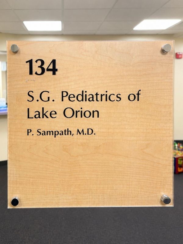 Office sign reading “134 S.G. Pediatrics of Lake Orion, P. Sampath, M.D.” on a wood plaque