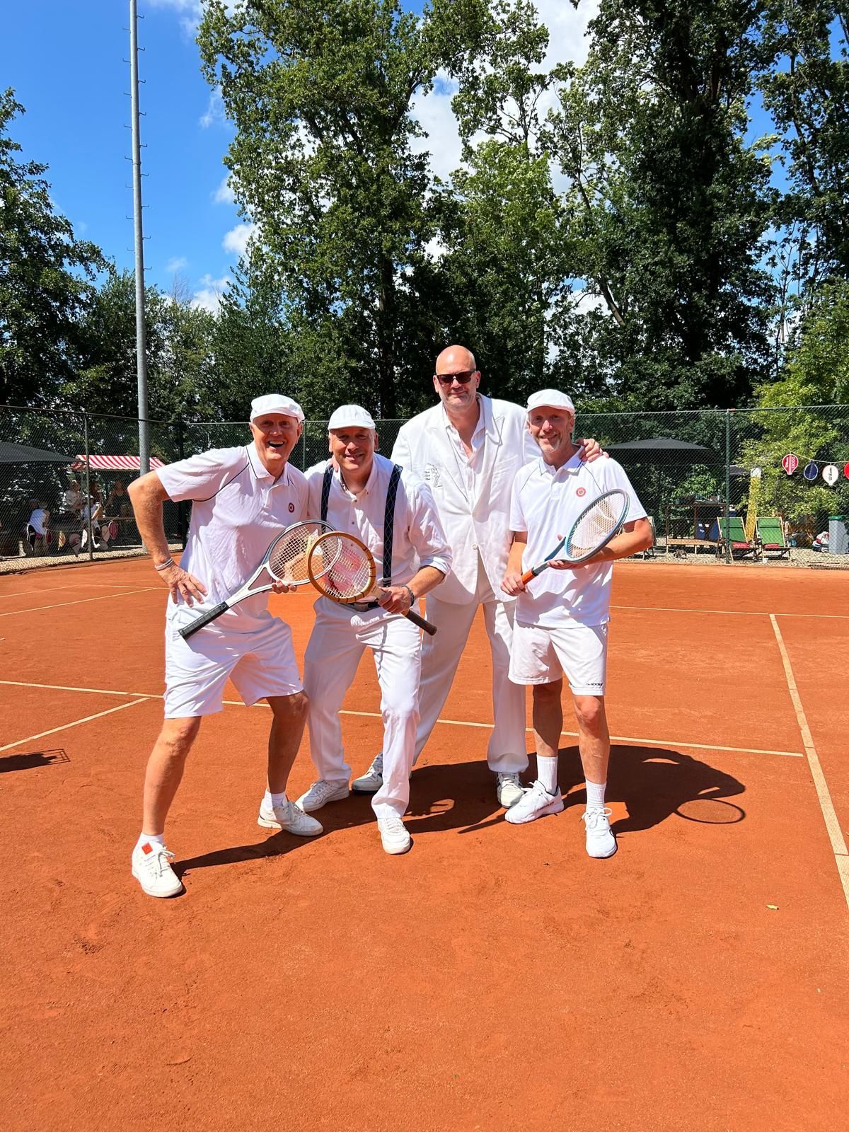 Vier classic geklede tennissers in ouderwets witte tenues poseren lachend en met de ouderwetse houten rackets 