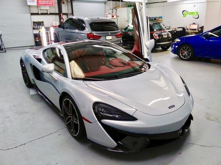 White McLaren sports car in a showroom, with a red interior and other cars in the background