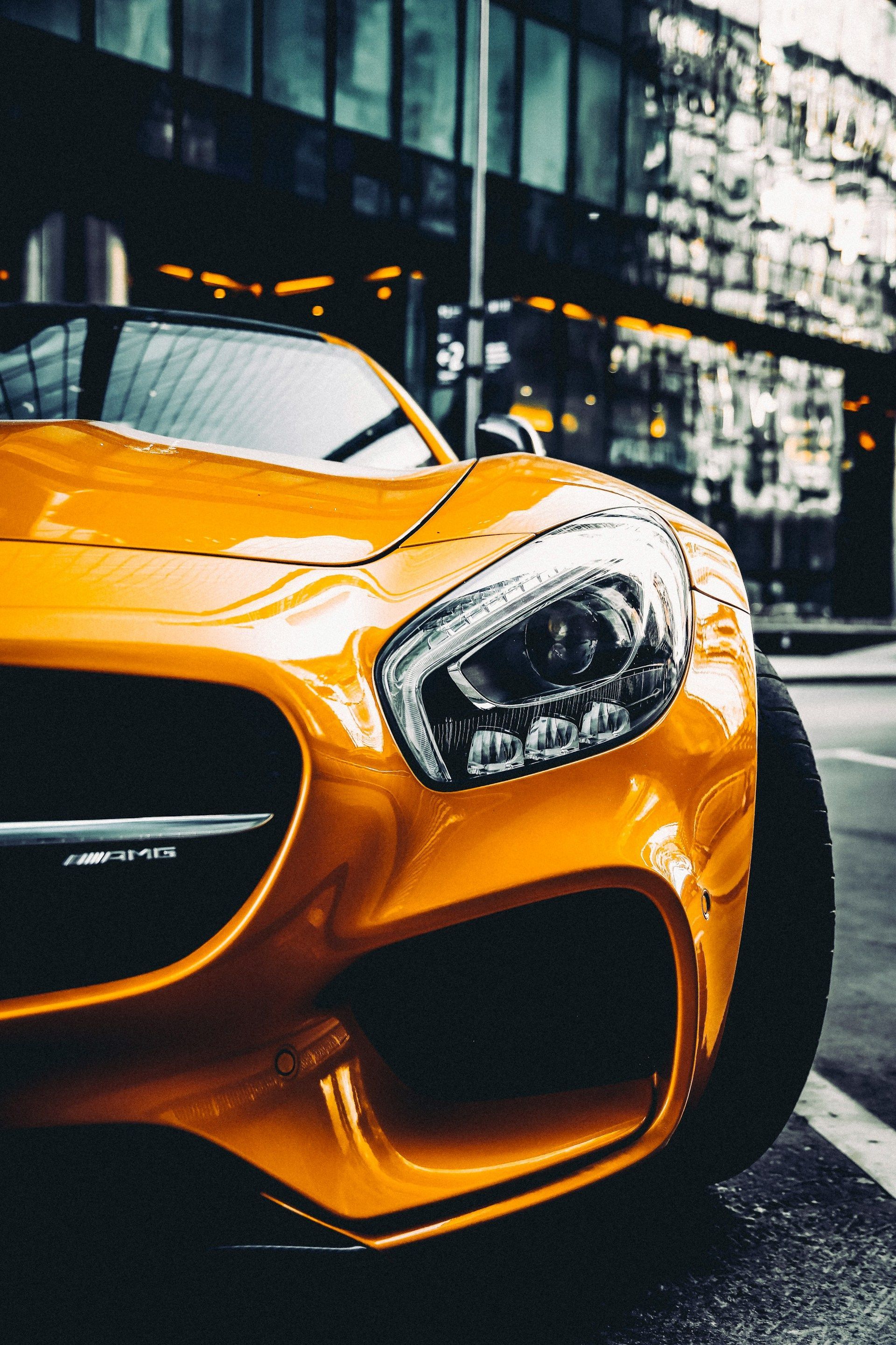 Close-up of an orange sports car parked on a city street, with a modern building in the background.