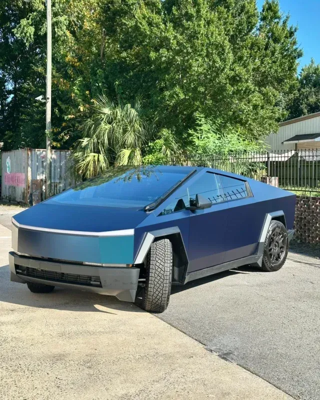 Blue Tesla Cybertruck parked outdoors in sunlight, angled front-left view.