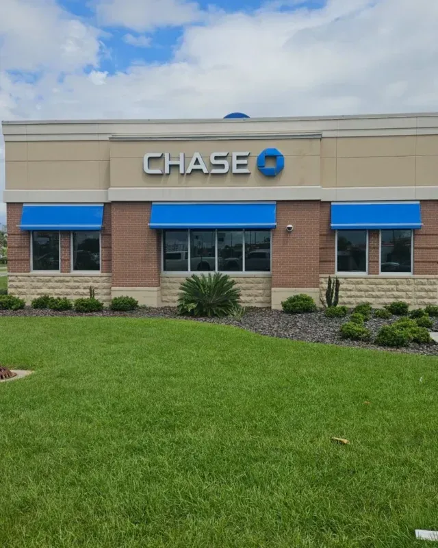 Chase bank branch exterior with beige and brick facade, blue awnings, and a green lawn in front.