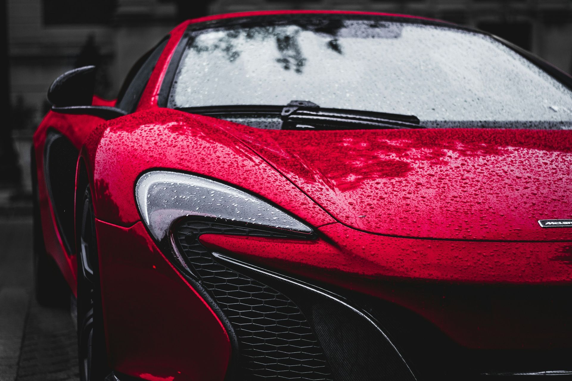 Red sports car front end covered in raindrops, close-up view