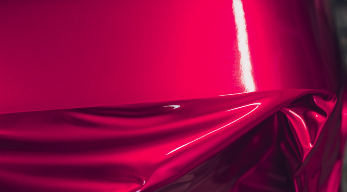 Abstract close-up of glossy hot pink satin fabric with folds and highlights