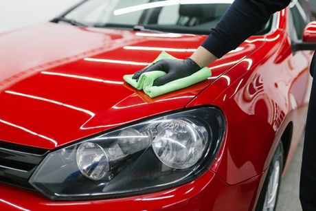 Person wiping a red car’s hood with a green cloth