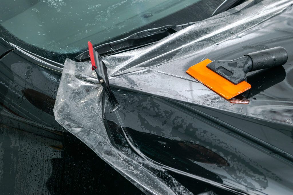 Close-up of a car windshield being scraped with an orange ice scraper, showing melting frost.