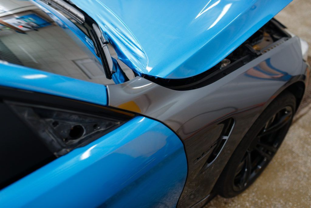 Close-up of a blue and black sports car with a damaged front panel and open hood