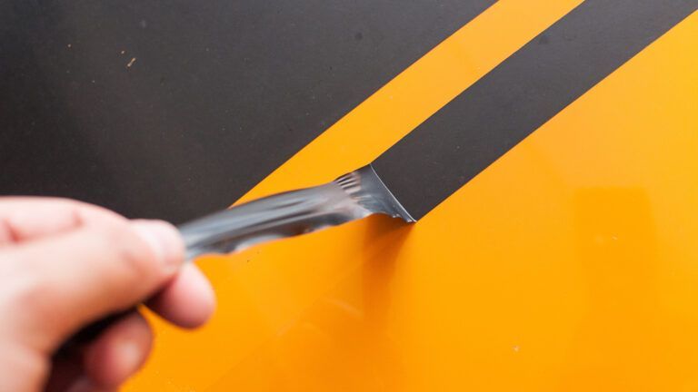 Hand peeling black tape from a glossy orange surface with diagonal black stripes
