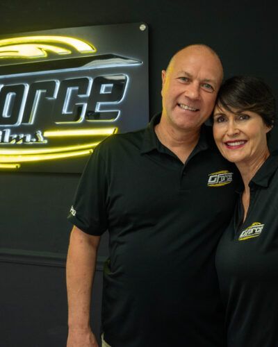 Two people in black polos smiling beside a glowing neon sign in a dark office lobby
