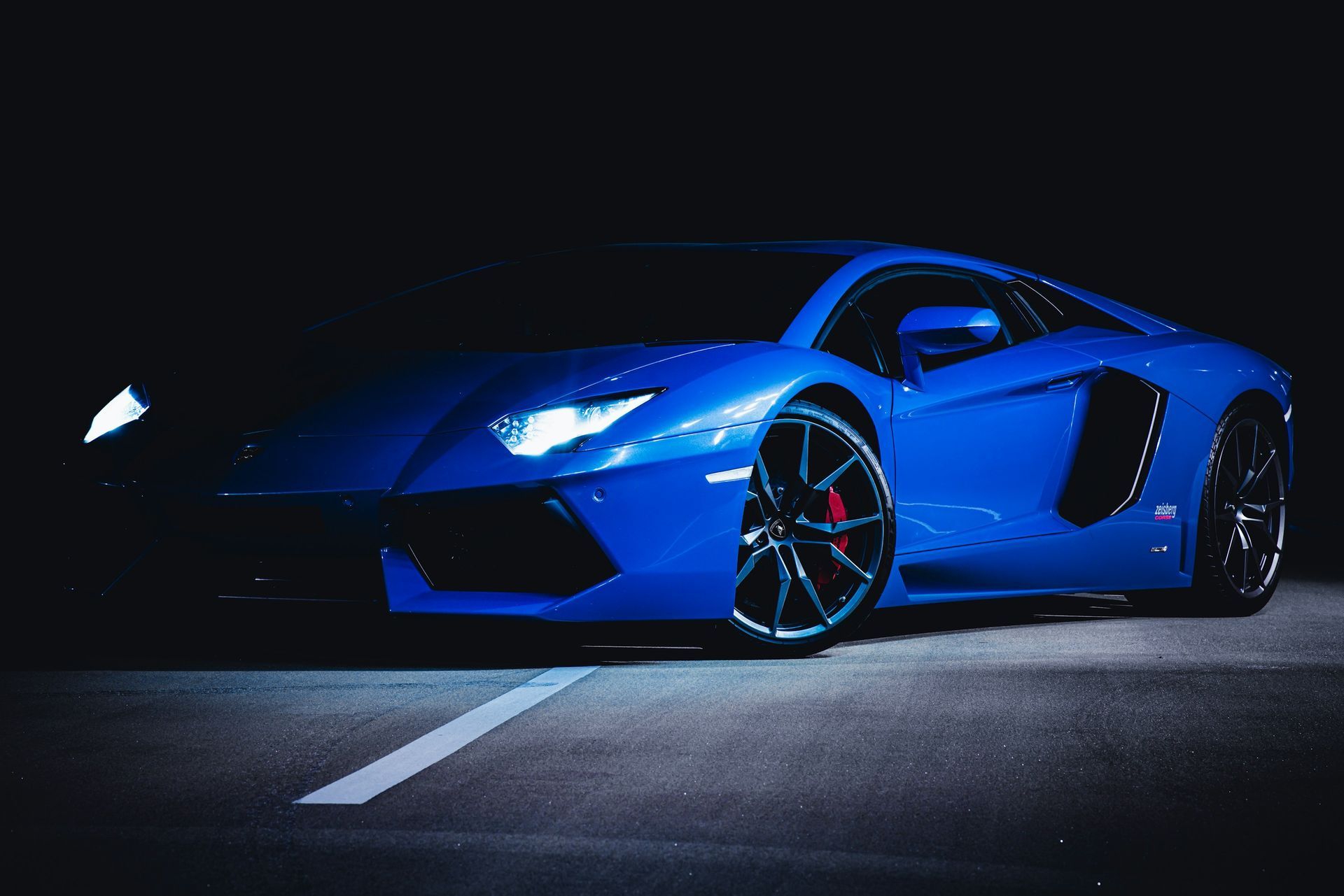 Blue sports car parked at night on a dark road, with bright headlights and a low, sleek body