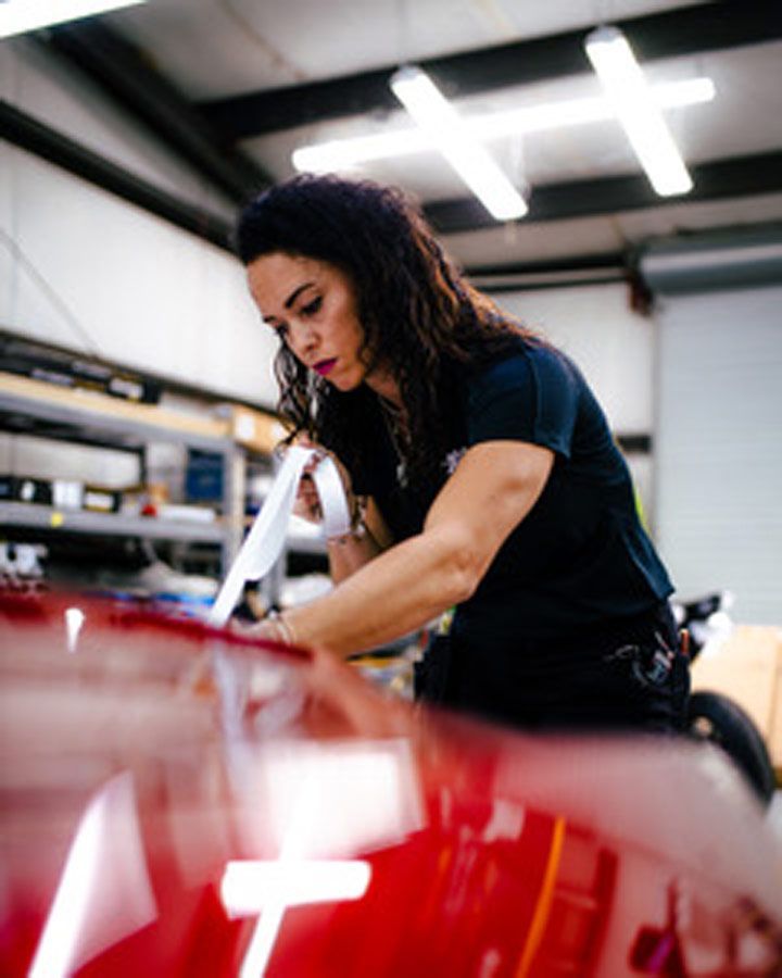 Mechanic polishing a red car in an auto shop, with bright overhead lights and shelves in the background