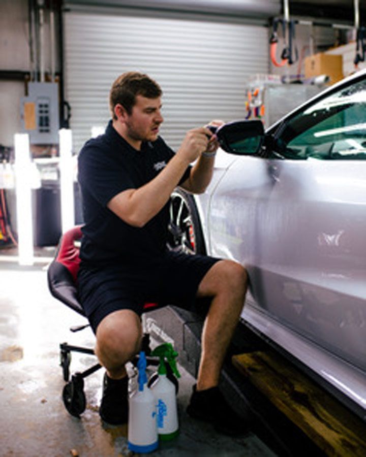 Detailer polishing a silver car door in a garage, with spray bottles and a stool nearby