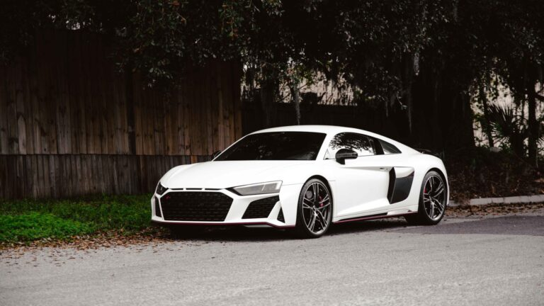 White sports car parked on a roadside beside a wooden fence and trees