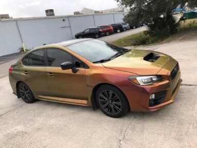 Orange and black customized sedan parked on a driveway beside a building