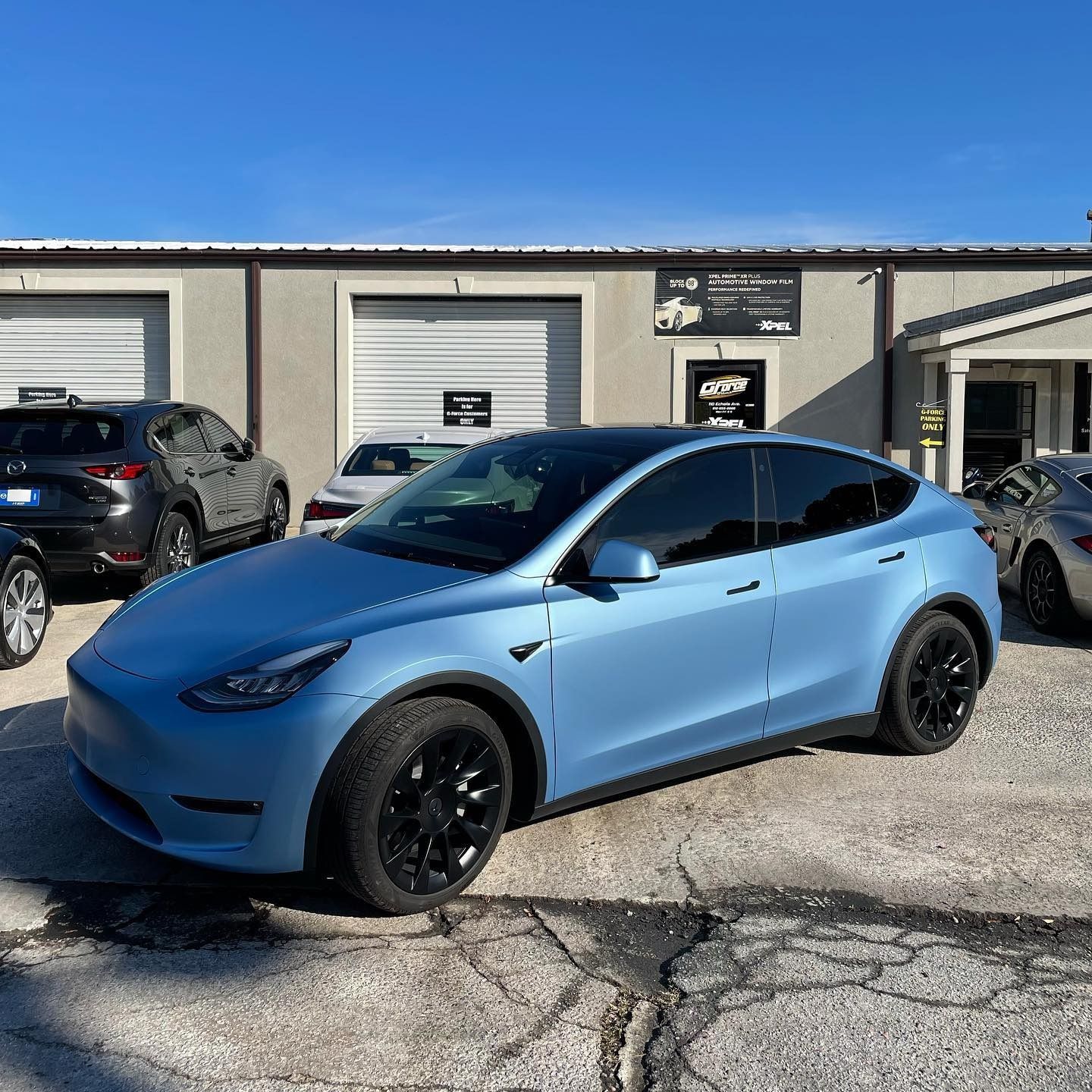 Blue Tesla Model Y parked outside a garage on a sunny day