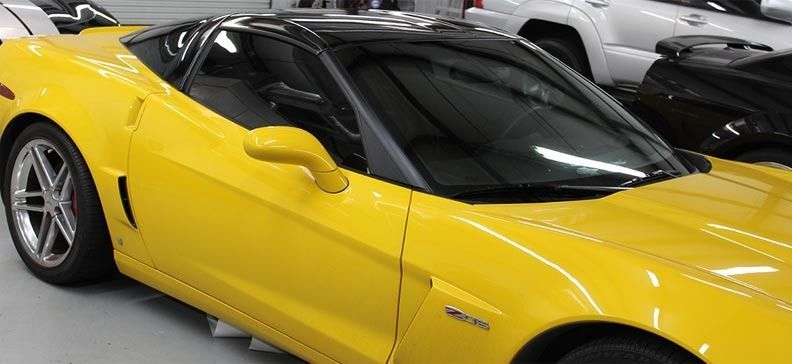 Yellow sports car in a showroom, angled front view with black roof and silver wheels