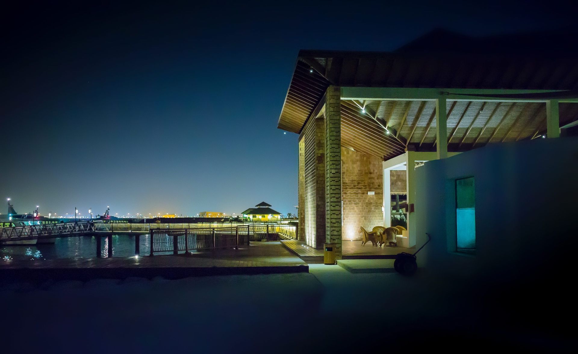 Nighttime waterfront terrace with modern lit pavilion and distant city skyline