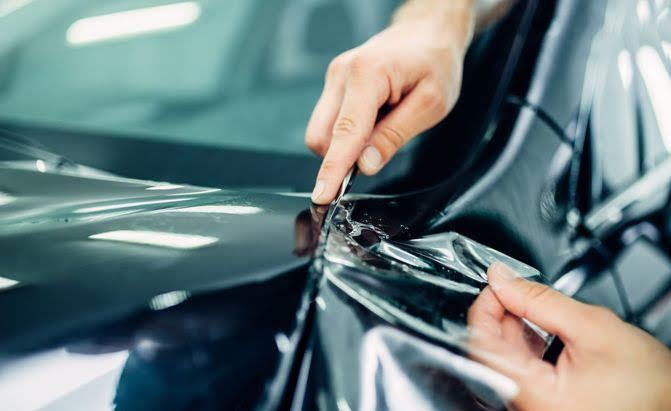 Hands applying clear protective film to a glossy dark green car surface