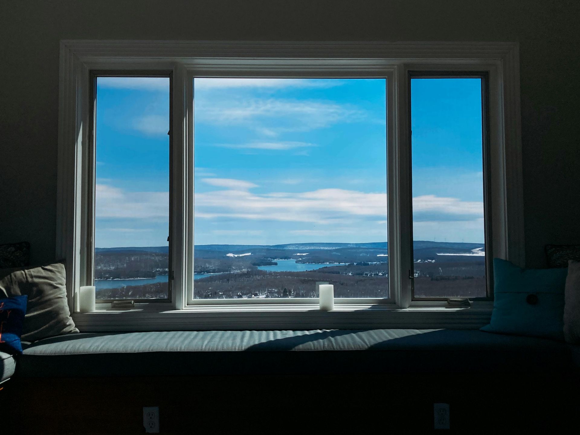 Window seat overlooking a bright blue sky and distant water, with a cushion-covered bench in the foreground