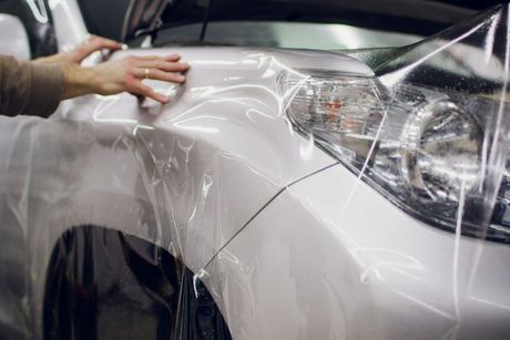 Hand applying clear protective film to a white car’s front fender and headlight